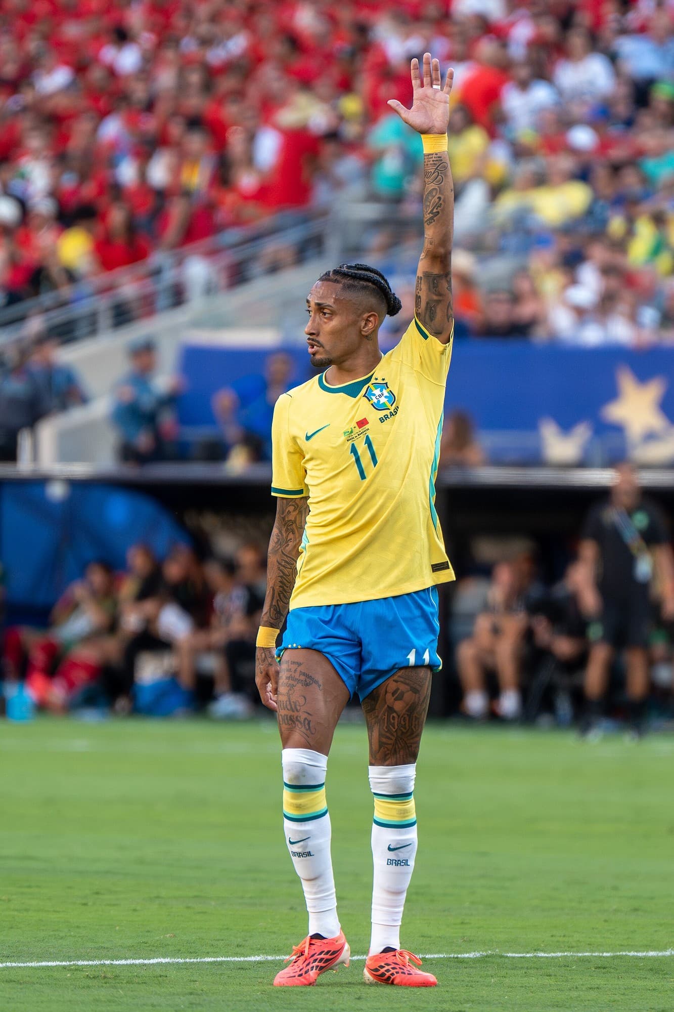 Raphinha me uniformën e verdhë të Brazilit në fushë, me njërin krah të ngritur.