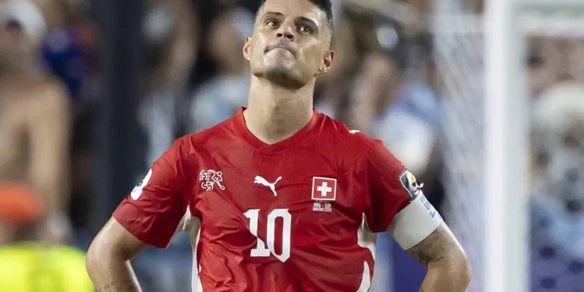 Granit Xhaka me fanellën e kuqe të Zvicrës dhe shiritin e kapitenit, me duart në ijë në fushë.