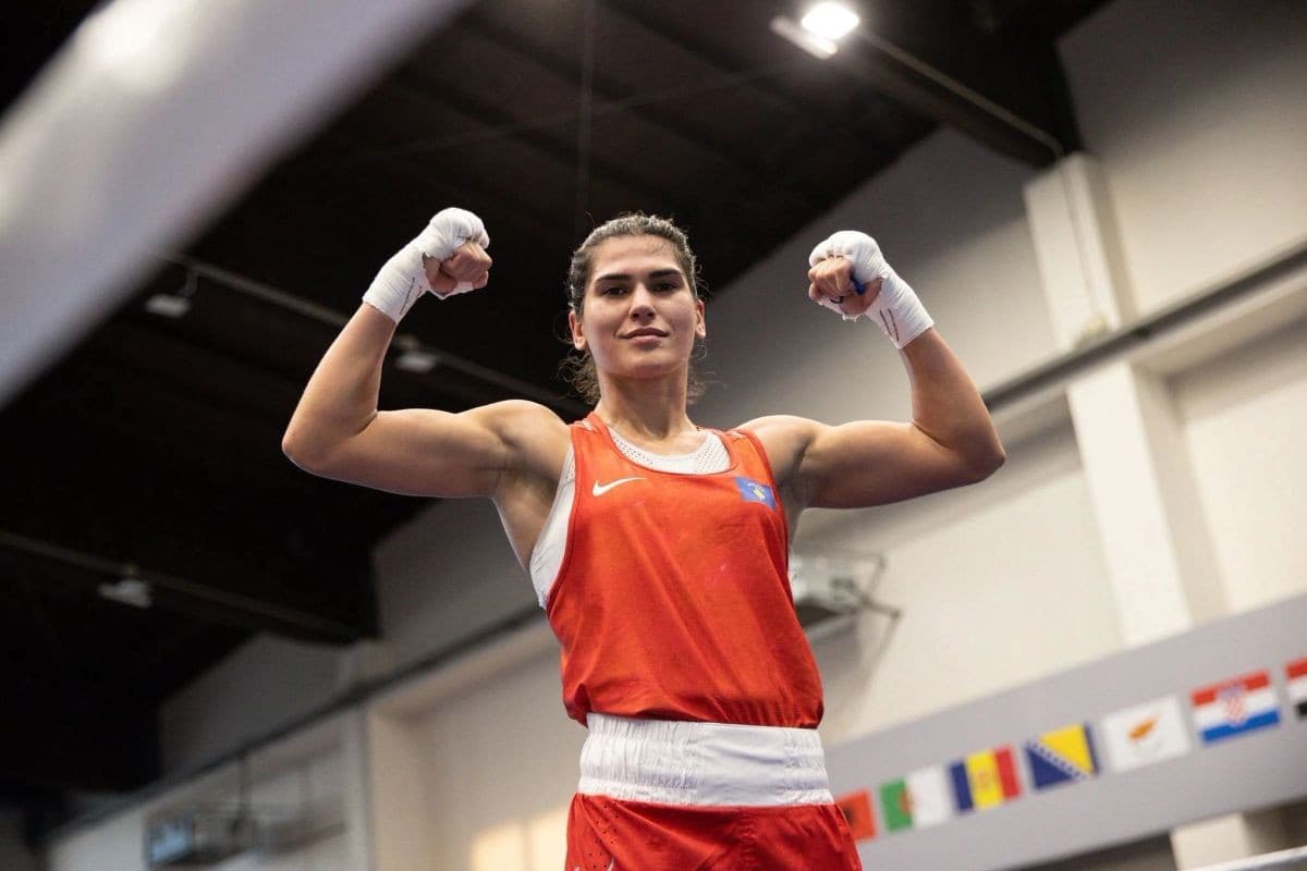 Donjeta Sadiku me veshje të kuqe boksi dhe duar të fashuara, duke mbajtur krahët lart në një sallë sportive.