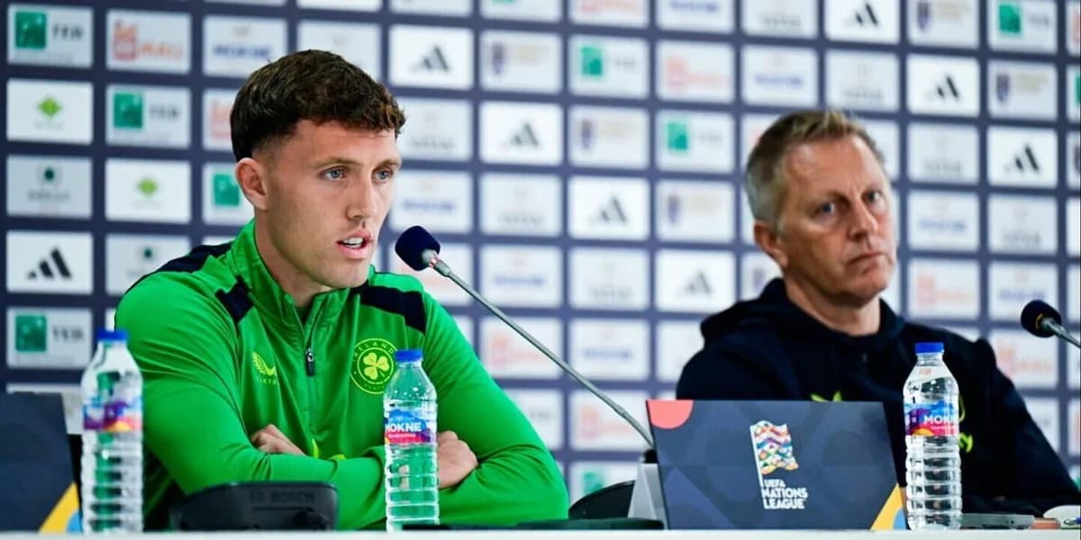 Dara O’Shea me veshje sportive të gjelbër në një konferencë për shtyp, me mikrofon përpara dhe një burrë tjetër në krah.