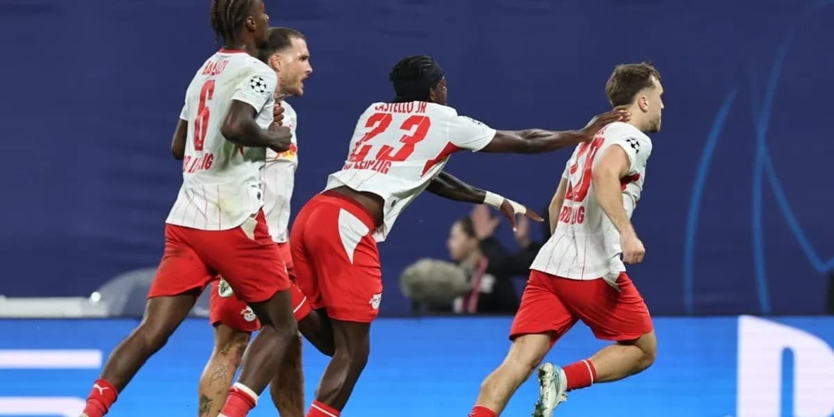 Futbollistë të RB Leipzigut me fanella të bardha dhe pantallona të kuqe vrapojnë në fushë.