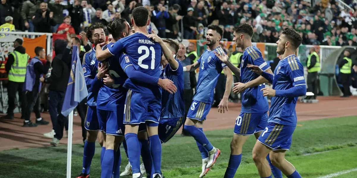 Futbollistë të Kosovës me fanella blu të mbledhur pranë flamurit të këndit në stadium.