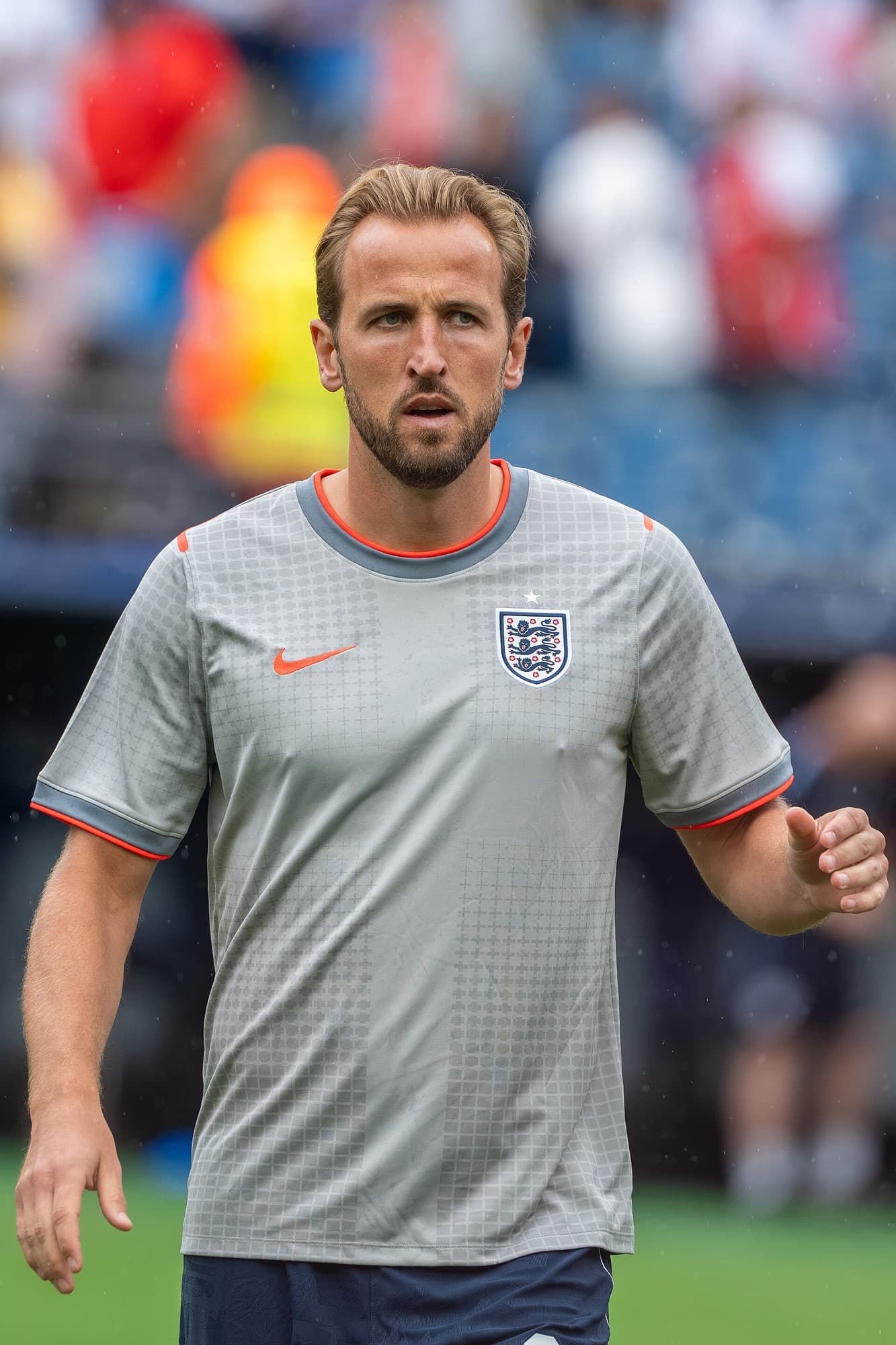 Harry Kane me fanellë gri të Anglisë në fushë; në sfond shihen tribuna të turbulluara.