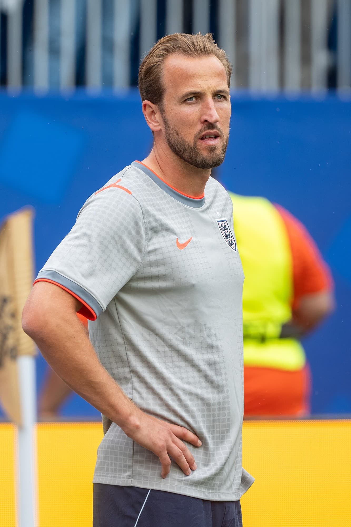 Harry Kane me bluzë gri të Anglisë, me njërën dorë në ijë.