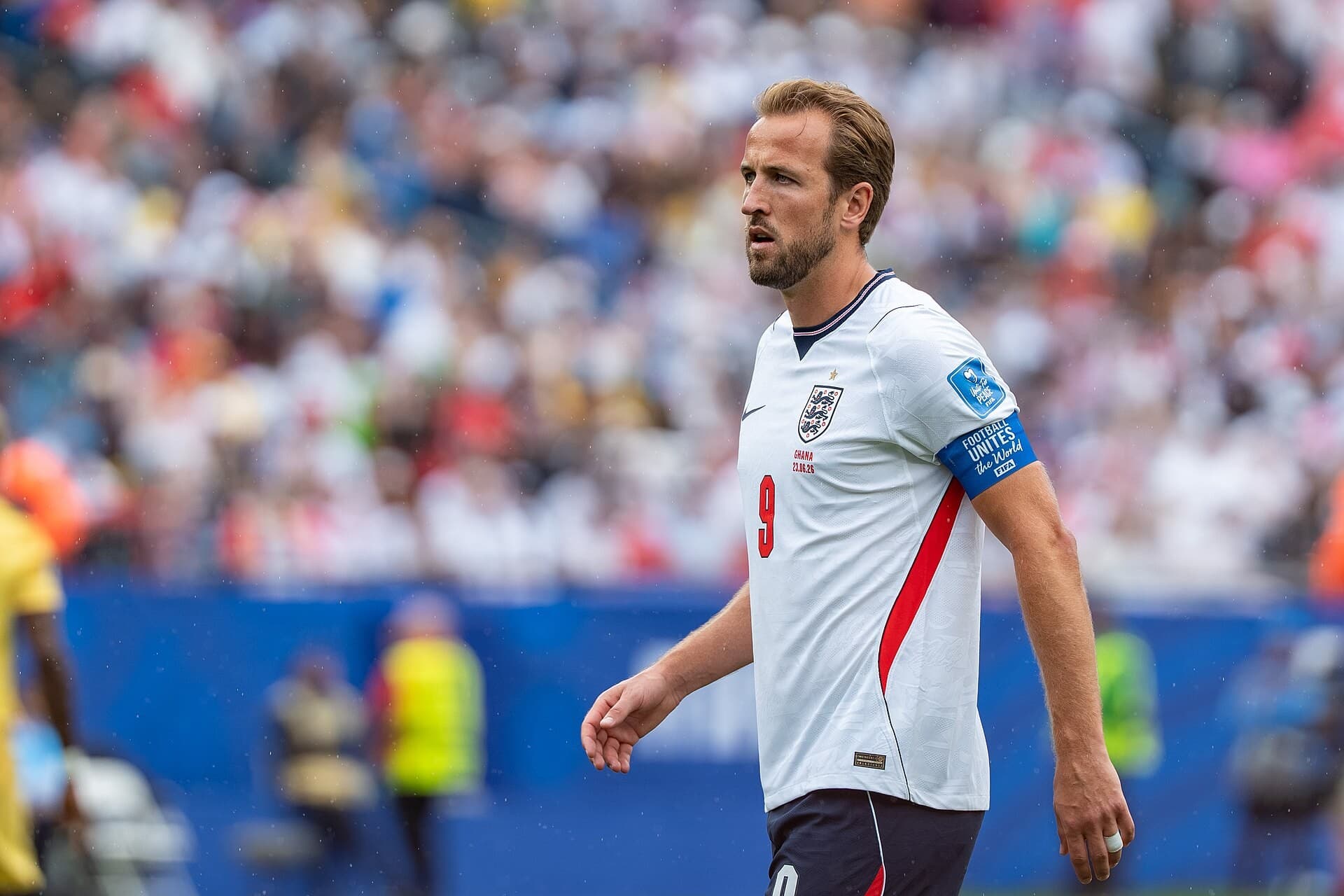 Harry Kane me fanellën e Anglisë në fushë, me tribuna të turbulluara në sfond.